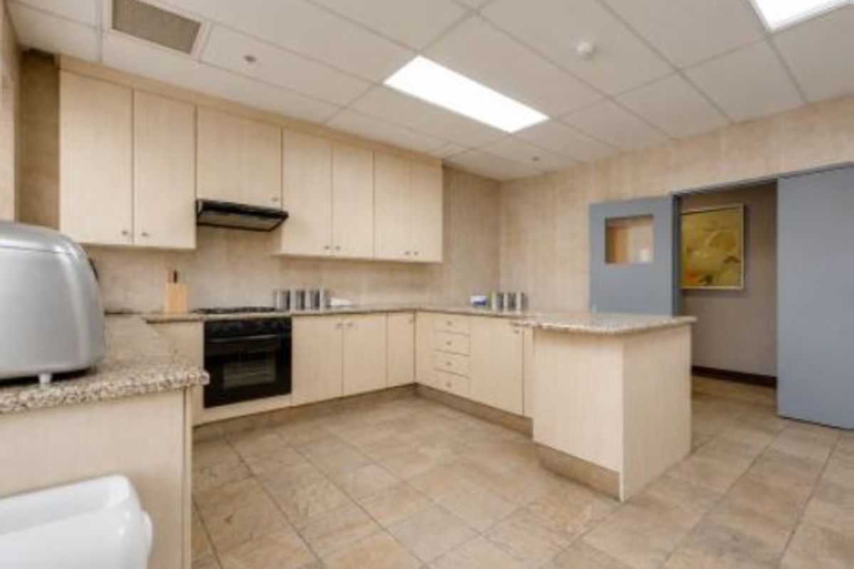 A functional commercial kitchen featuring light wood cabinetry, granite countertops, integrated oven, extractor fan, and durable tiled flooring with recessed ceiling lighting.