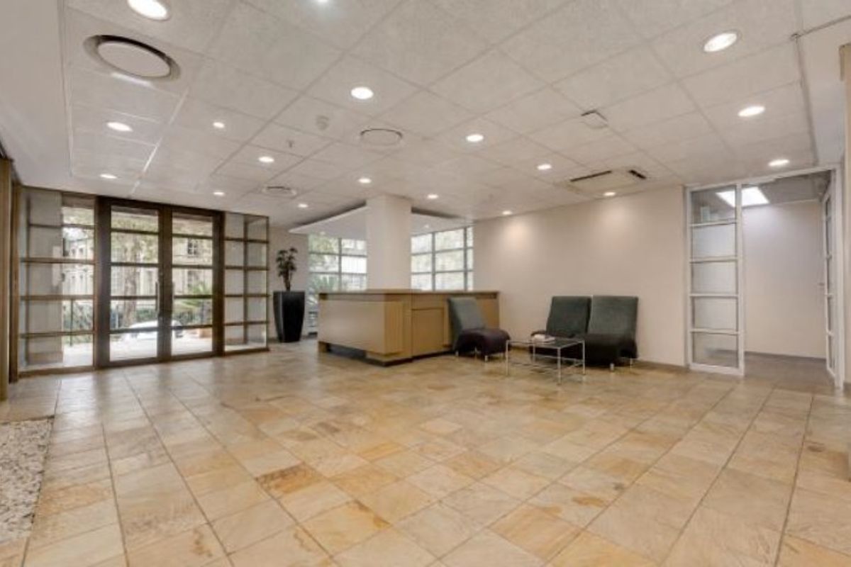 Spacious commercial reception area featuring stone tile flooring, a built-in reception desk, suspended ceiling with recessed lighting, and large glass entrance doors.
