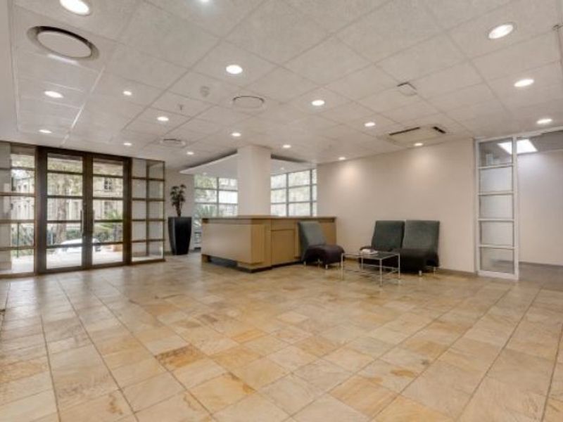Spacious commercial reception area featuring stone tile flooring, a built-in reception desk, suspended ceiling with recessed lighting, and large glass entrance doors.