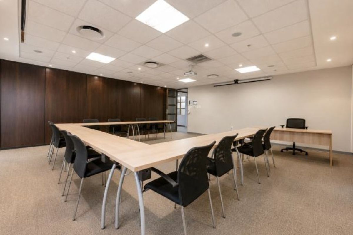A professional commercial boardroom featuring wood paneling, carpeted flooring, a suspended ceiling with recessed lighting, and an integrated projector system.