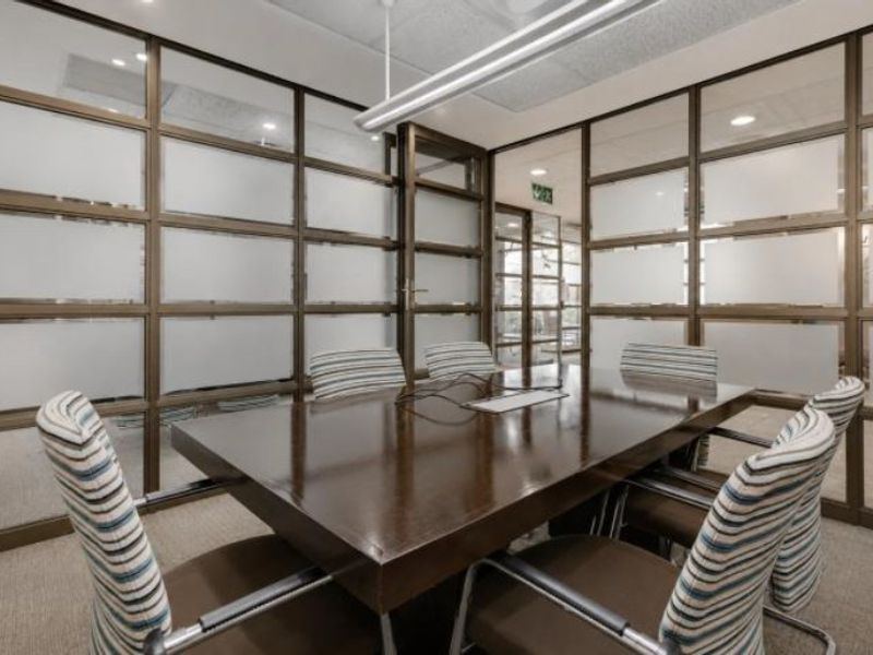 A professional meeting room featuring modern glass partition walls, suspended ceiling with linear lighting, and carpeted flooring.