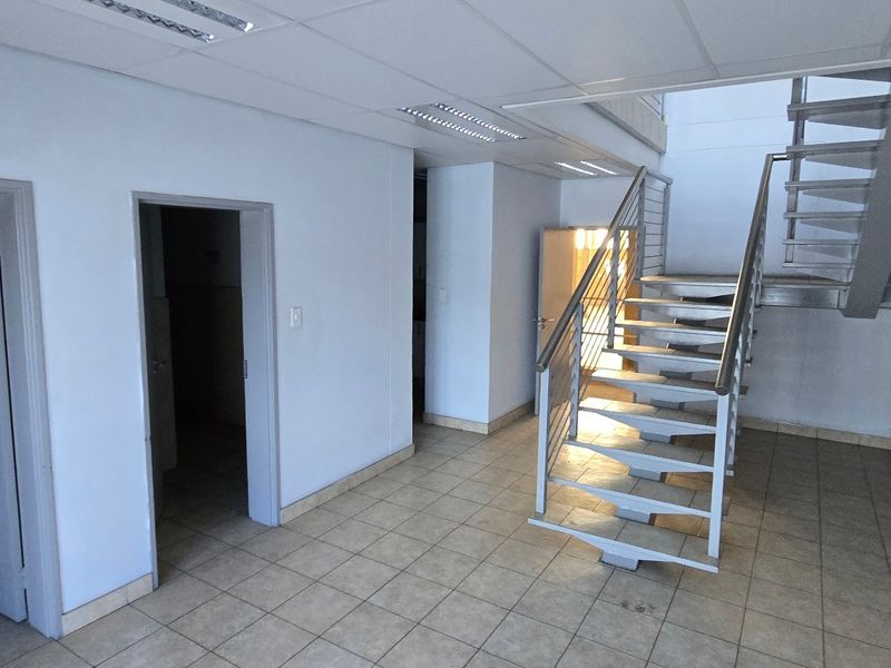 A spacious industrial hallway featuring tiled flooring, a modern metal staircase with stainless steel handrails, and a suspended ceiling with recessed lighting.