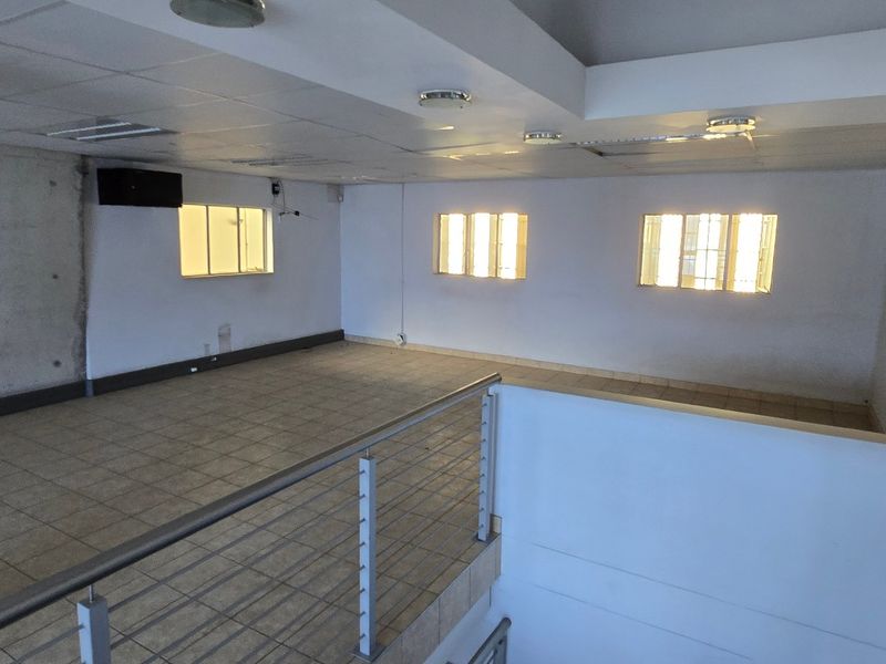 Spacious open-plan industrial mezzanine area featuring tiled flooring, an exposed concrete feature wall, and a secure metal balustrade overlooking the lower level.