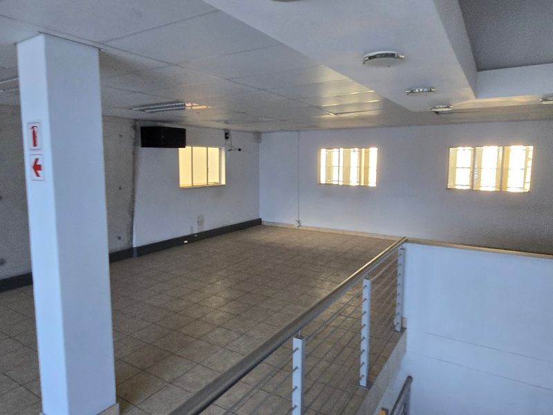 An open-plan industrial space featuring tiled flooring, a concrete feature wall, suspended ceilings, and a metal balustrade overlooking the lower level.