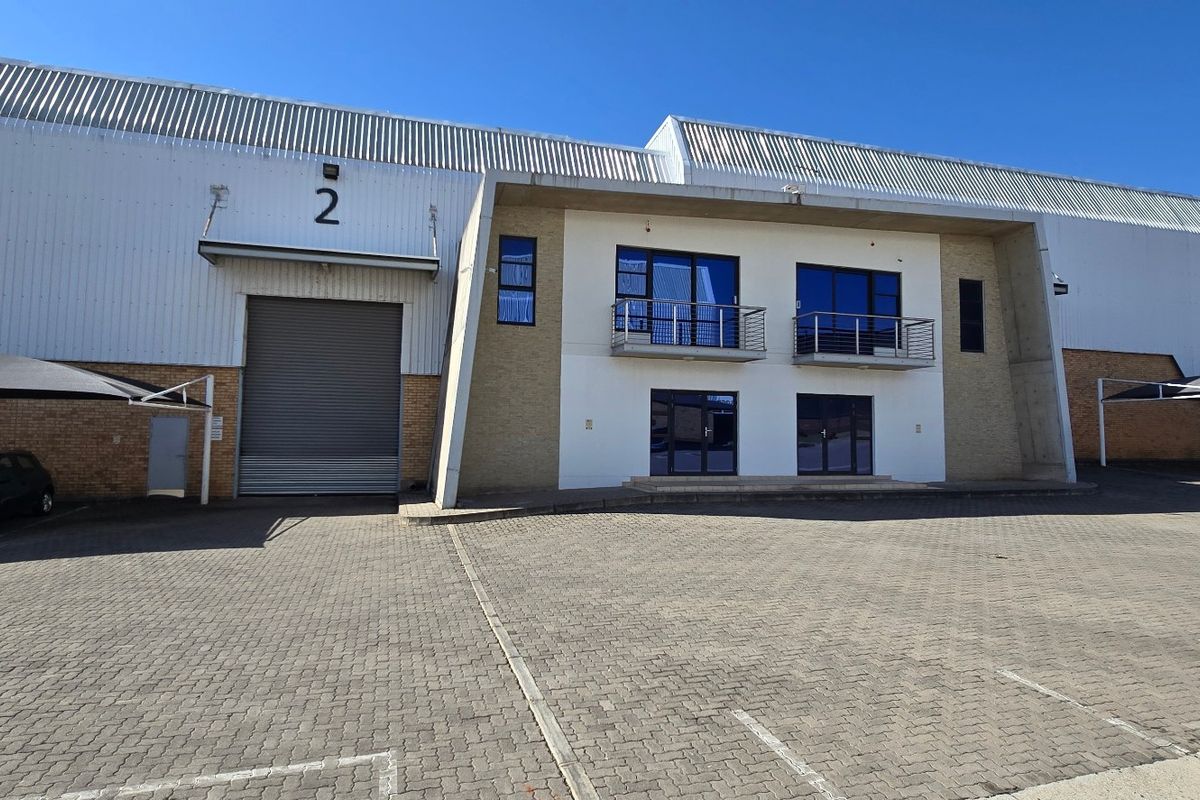 Front elevation of an industrial warehouse facility featuring a large roller shutter door, office section with balconies, and paved parking with shade cloth carports.