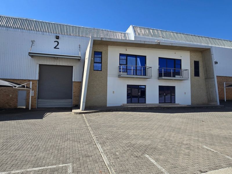 Front elevation of an industrial warehouse facility featuring a large roller shutter door, office section with balconies, and paved parking with shade cloth carports.