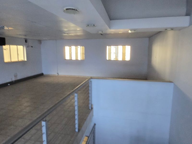 An open-plan mezzanine office space featuring tiled flooring, recessed lighting, and a metal balustrade overlooking the lower level.