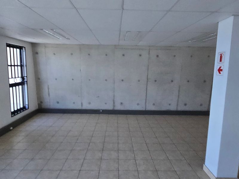 An open-plan industrial office space featuring tiled flooring, a prominent exposed concrete feature wall, and a suspended ceiling with integrated lighting.