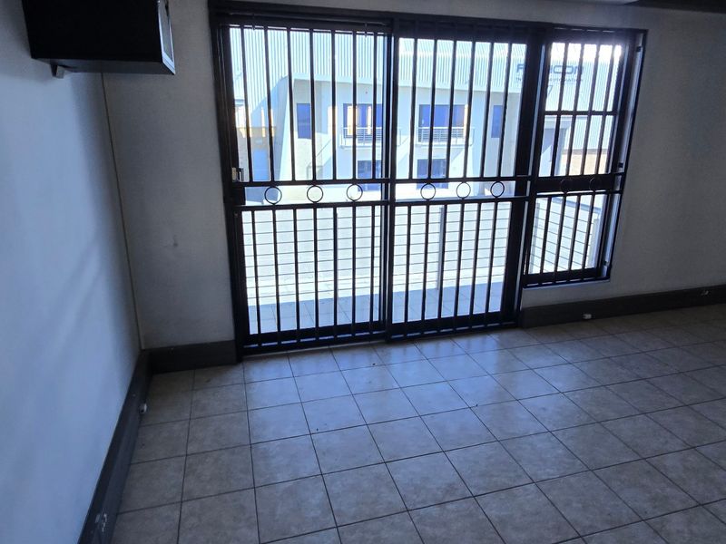 An empty office space featuring tiled flooring, security gates on the sliding doors, and neutral wall finishes.