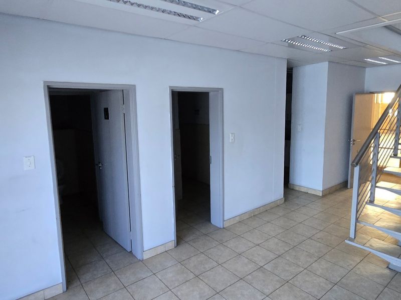 Industrial hallway featuring ceramic tiled flooring, a metal staircase with stainless steel handrails, and recessed ceiling lighting, providing access to multiple rooms.