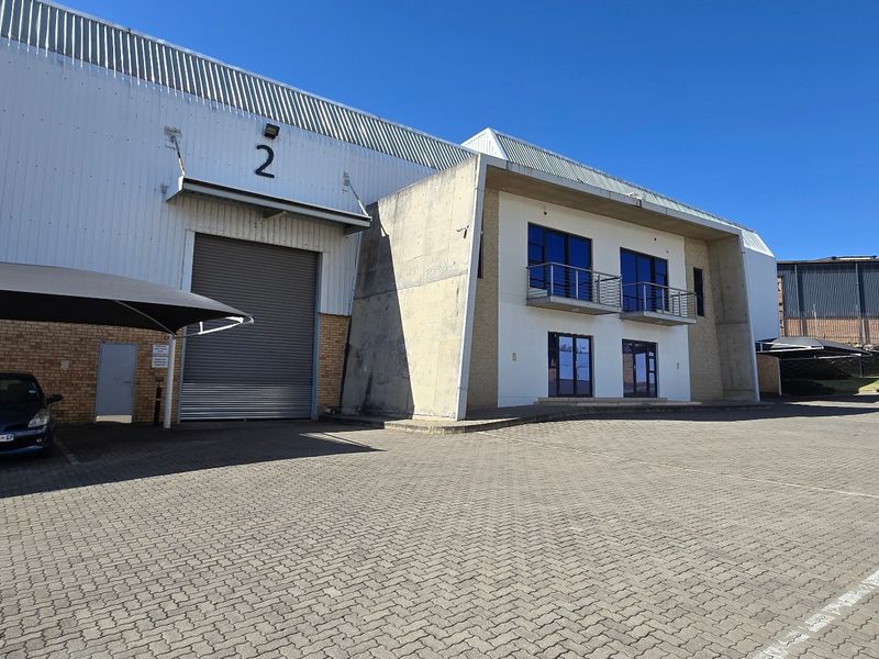 Industrial warehouse facility featuring a large roller shutter door, paved parking area, shade cloth carport, and a multi-level office section with balconies.