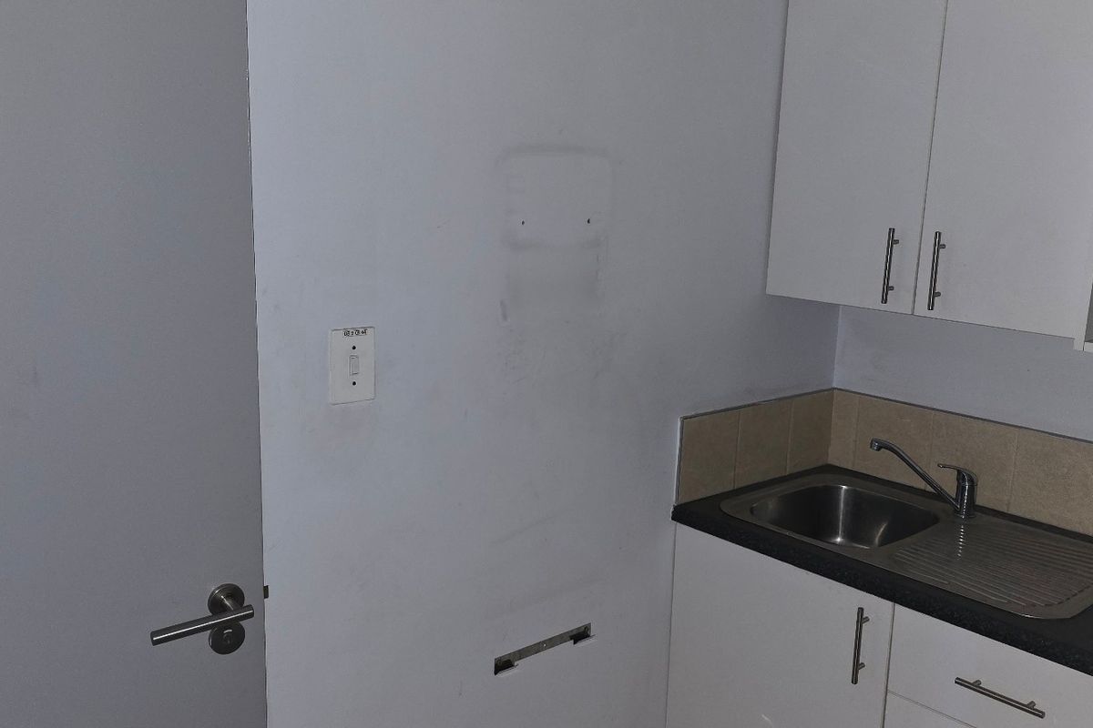 A small kitchenette area featuring white cabinetry, a stainless steel sink, and a tiled backsplash, adjacent to an accessible doorway.