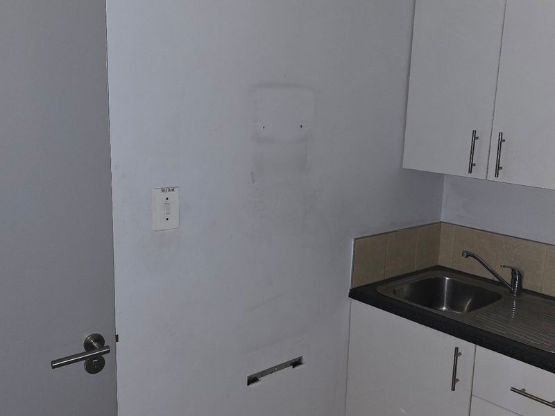 A small kitchenette area featuring white cabinetry, a stainless steel sink, and a tiled backsplash, adjacent to an accessible doorway.