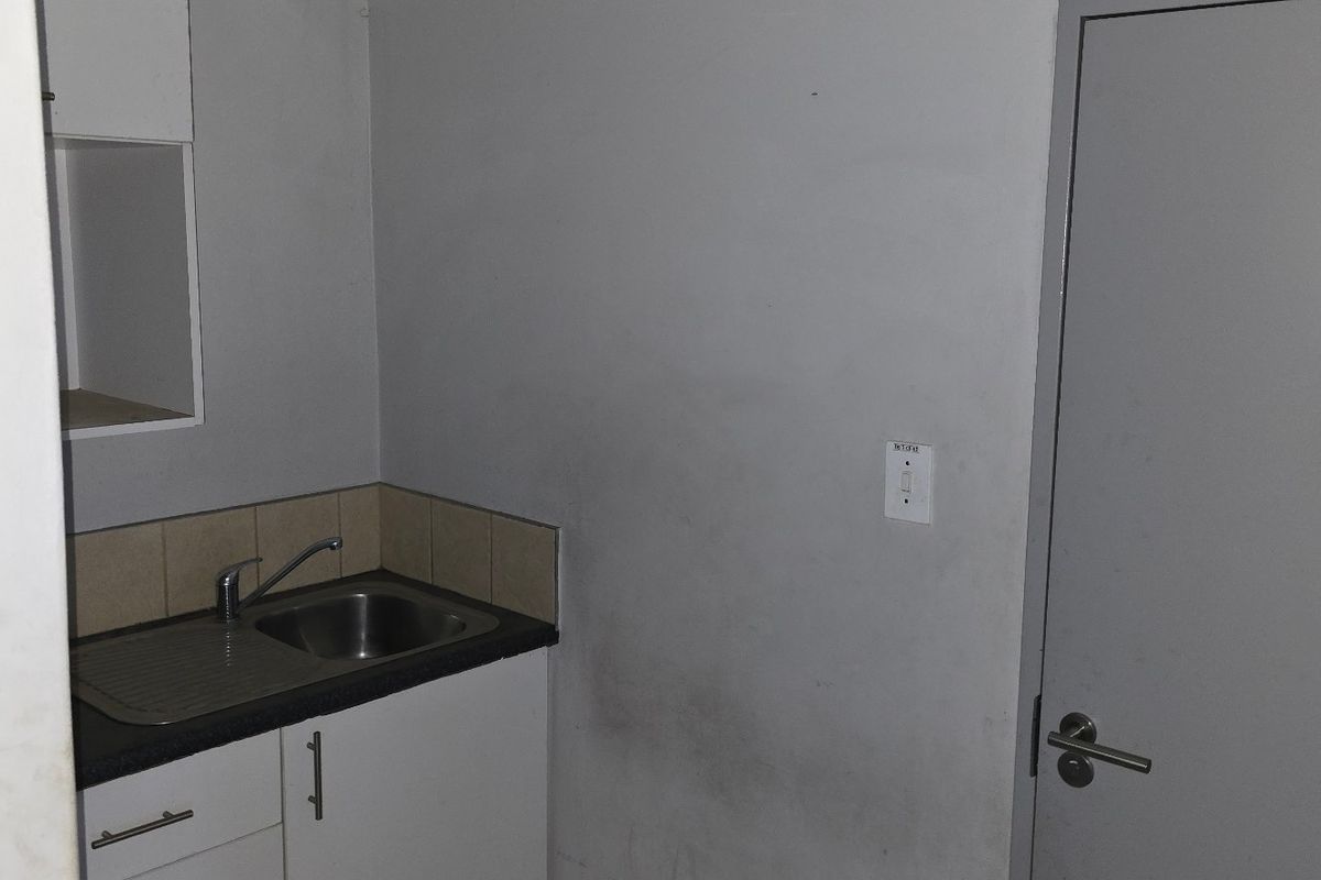 A small industrial kitchenette featuring a stainless steel sink, base cabinetry, and tiled splashback, adjacent to an accessible restroom door.
