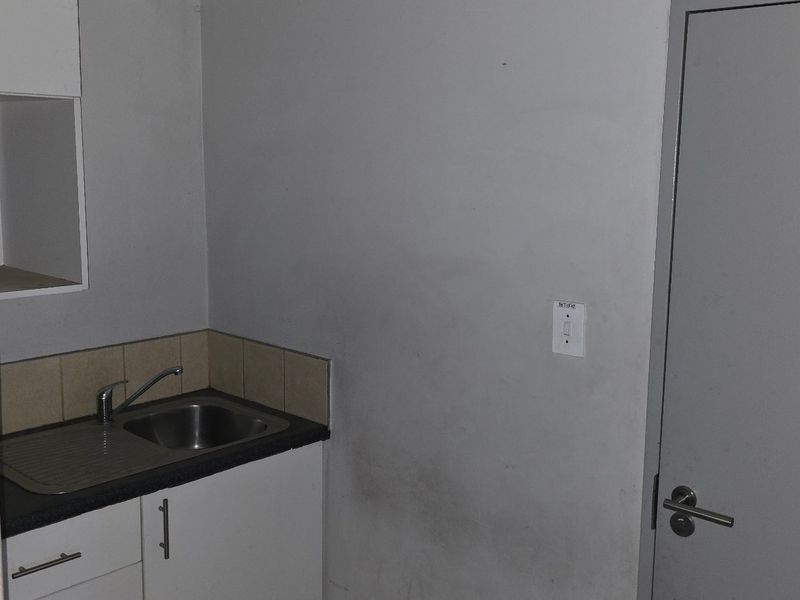A small industrial kitchenette featuring a stainless steel sink, base cabinetry, and tiled splashback, adjacent to an accessible restroom door.