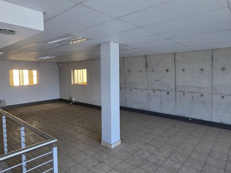 Spacious open-plan industrial office area featuring a prominent exposed concrete feature wall, tiled flooring, suspended ceiling, and a modern metal balustrade.