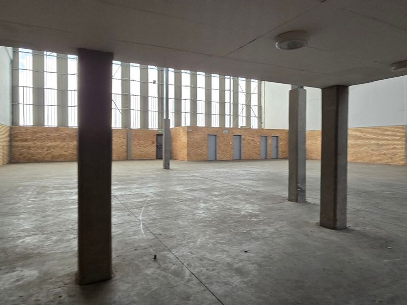 A spacious, empty industrial utility area featuring concrete flooring, exposed brick walls, and large industrial windows providing ample natural light.