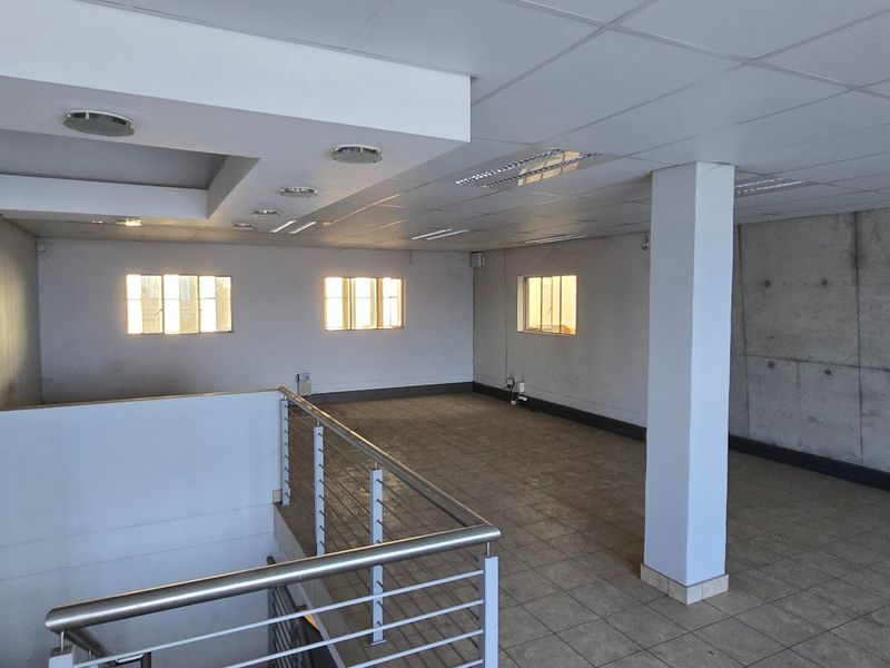 Spacious open-plan industrial office area featuring a suspended ceiling, tiled flooring, and a prominent exposed concrete feature wall.