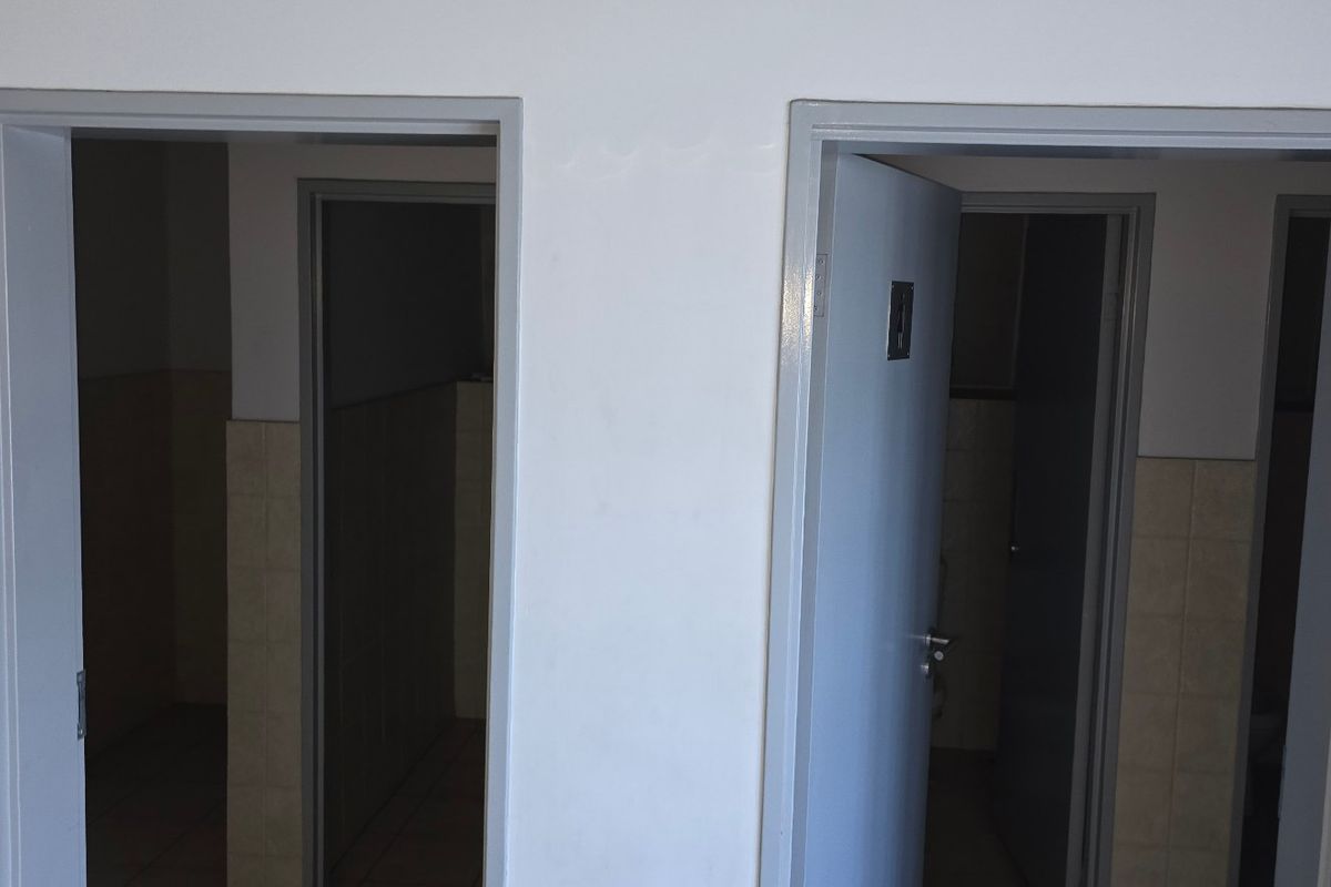A view of a hallway featuring two doorways leading into adjacent rooms with tiled wall finishes and standard light switches.