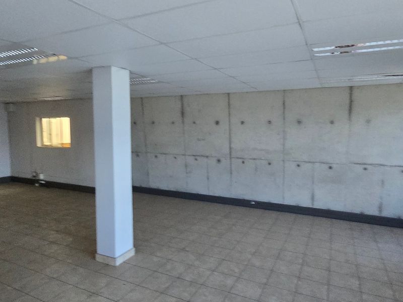 Spacious open-plan industrial office area featuring a prominent exposed concrete wall, tiled flooring, and suspended ceiling with integrated lighting.