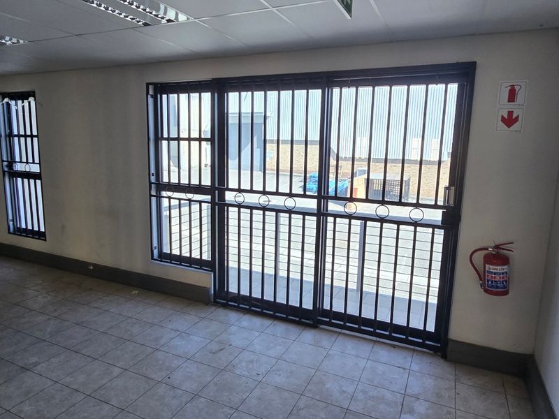 Empty industrial office space featuring tiled flooring, suspended ceiling with recessed lighting, and secure metal security gates on windows and doors.