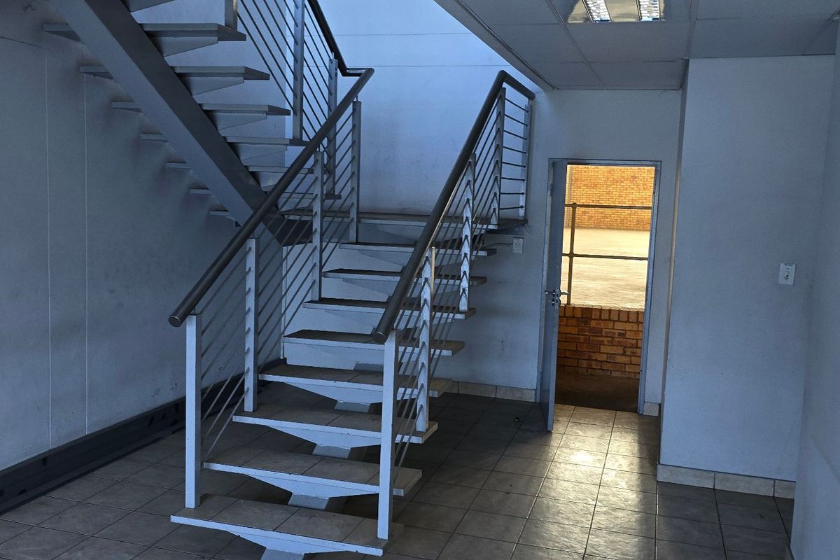 Industrial hallway featuring a metal staircase with stainless steel handrails, tiled flooring, and access to an exterior area.