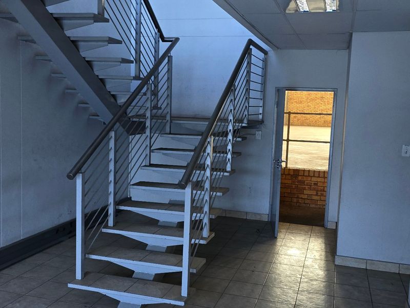 Industrial hallway featuring a metal staircase with stainless steel handrails, tiled flooring, and access to an exterior area.