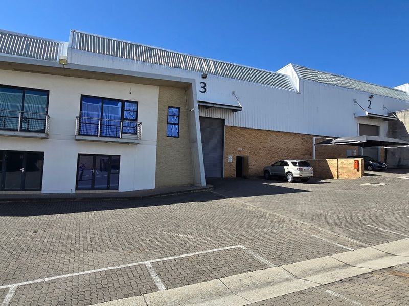 Front elevation of an industrial warehouse complex featuring roller shutter doors, paved parking area, and upper-level office balconies.