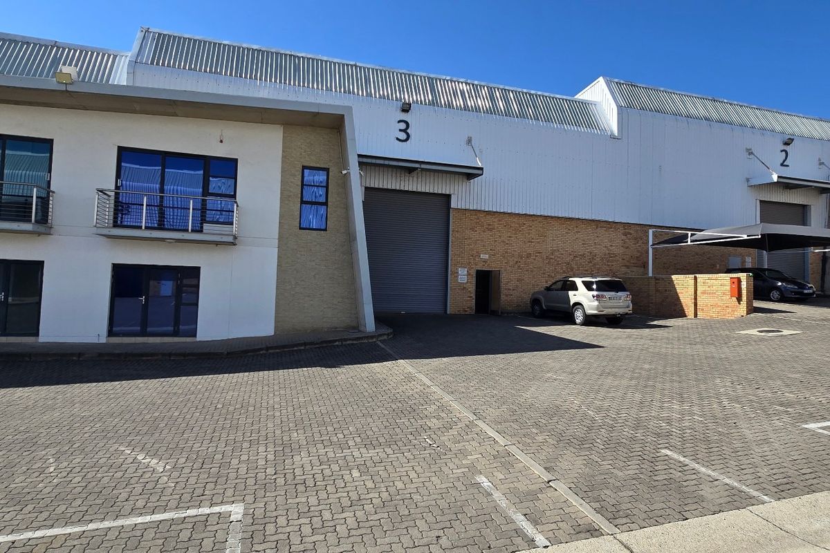 Front elevation of an industrial warehouse complex featuring roller shutter doors, brick and metal cladding, and paved parking area.