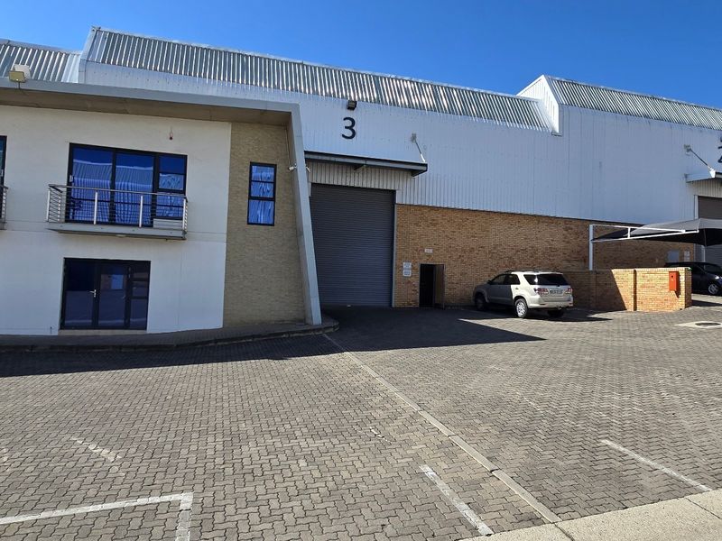 Front elevation of an industrial warehouse complex featuring roller shutter doors, brick and metal cladding, and paved parking area.