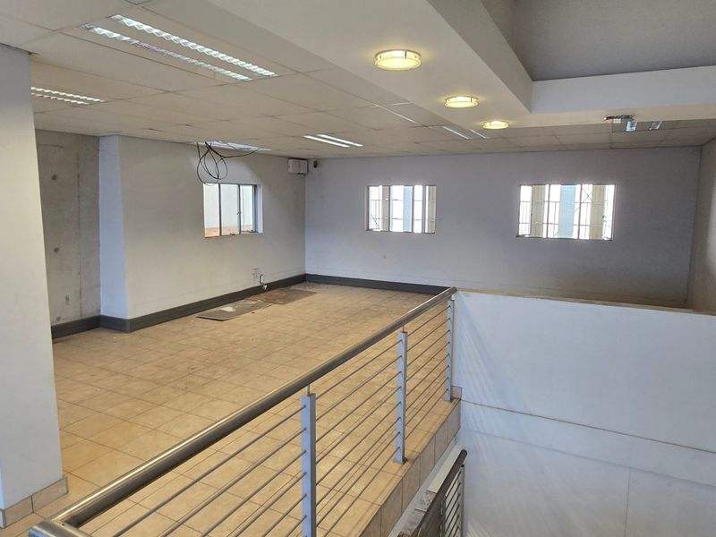 Open-plan office mezzanine area featuring tiled flooring, recessed lighting, and a metal balustrade overlooking the lower level.
