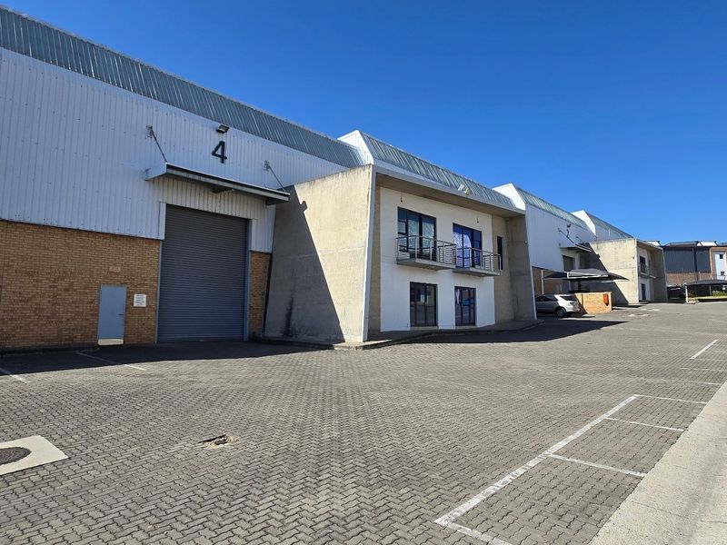 Industrial warehouse unit featuring a large roller shutter door, brick and metal facade, and dedicated paved parking area in a commercial complex.