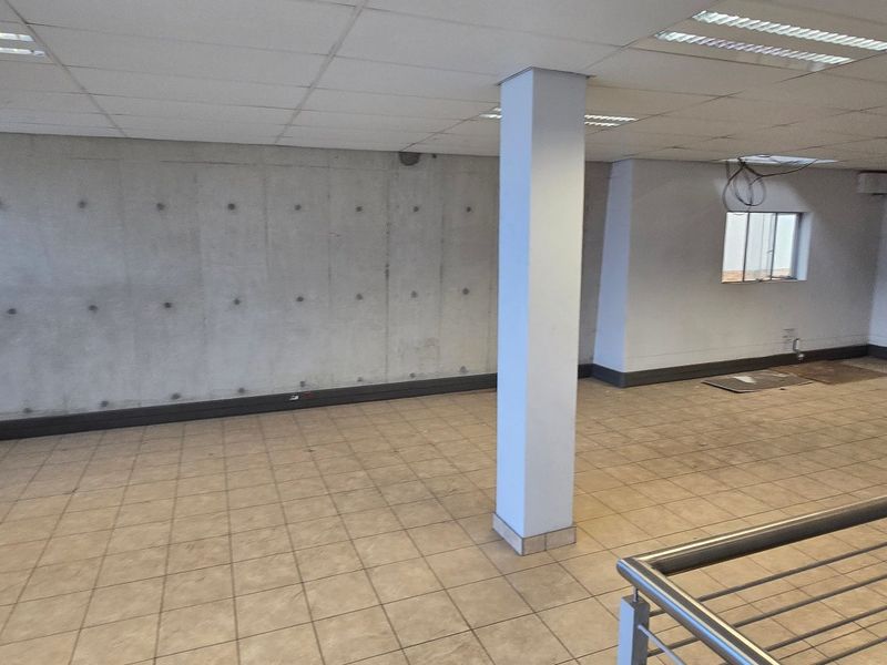 Spacious open-plan industrial office area featuring exposed concrete walls, ceramic tiled flooring, suspended ceilings, and a metal balustrade overlooking the lower level.