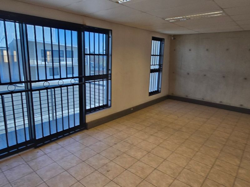 An empty industrial office space featuring tiled flooring, an exposed concrete feature wall, and security bars on the sliding door and windows.