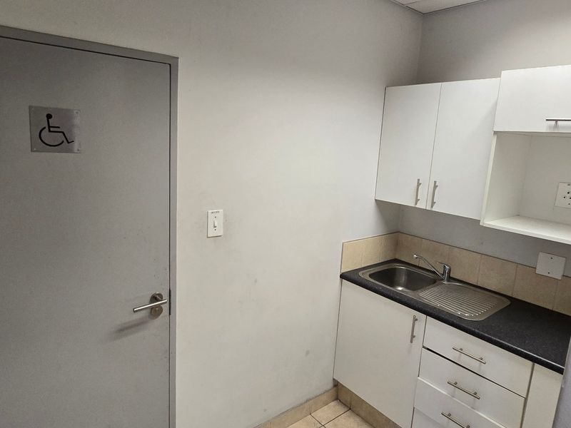 A compact kitchenette featuring white built-in cabinetry, a stainless steel sink, and a dark laminate countertop, adjacent to an accessible doorway.