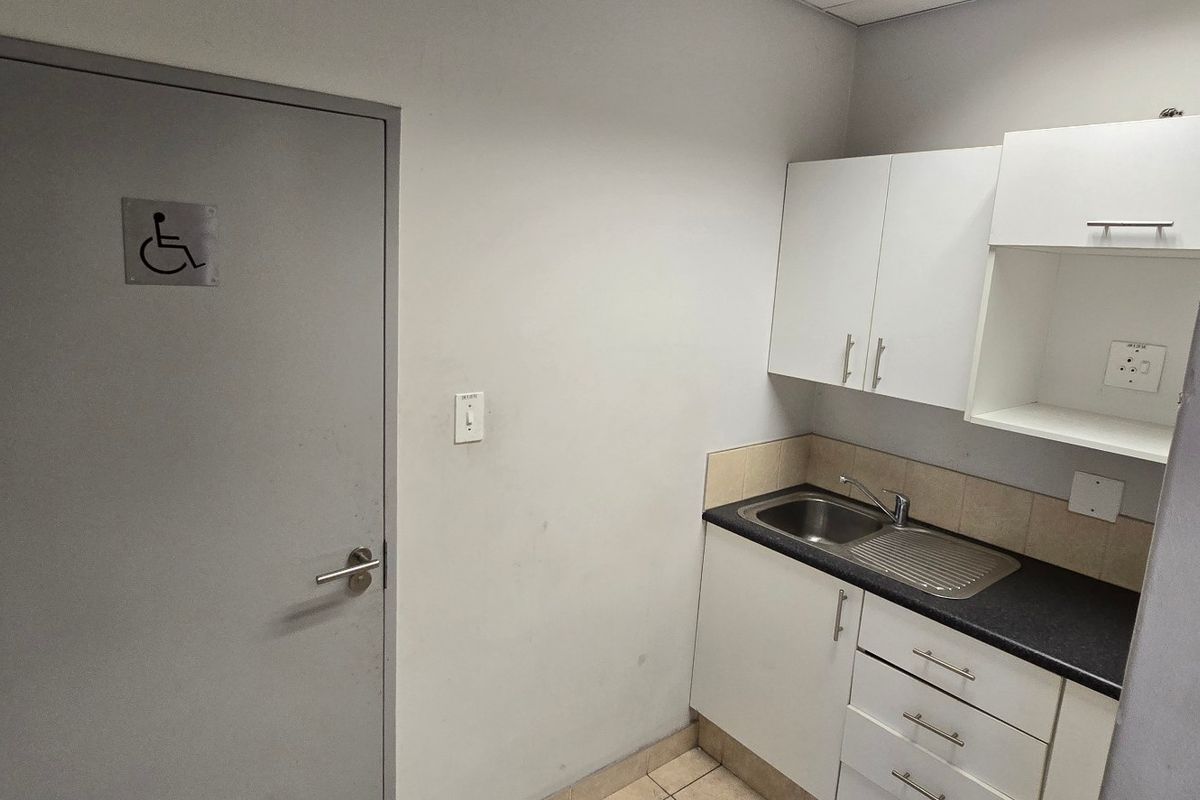 A compact kitchenette featuring white built-in cabinetry, a stainless steel sink, and a dark laminate countertop, adjacent to an accessible doorway.