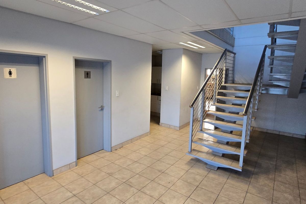 A clean, functional industrial hallway featuring tiled flooring, a modern metal staircase, and access to multiple internal rooms.