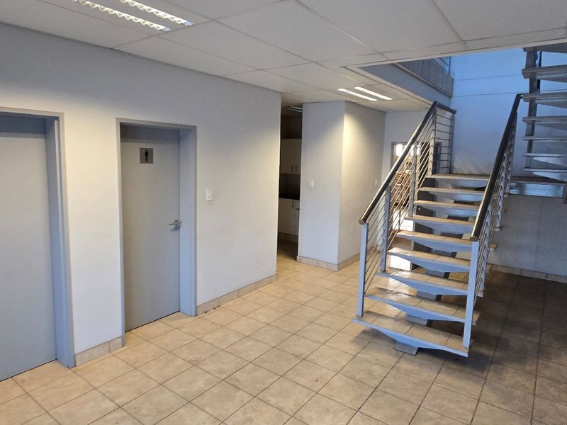 A clean, functional industrial hallway featuring tiled flooring, a modern metal staircase, and access to multiple internal rooms.