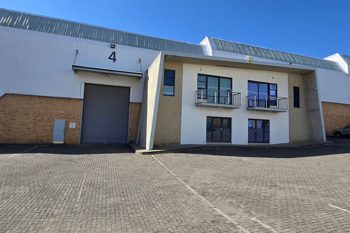 Front elevation of an industrial warehouse unit featuring a large roller shutter door, brick and metal cladding, and integrated office balconies.