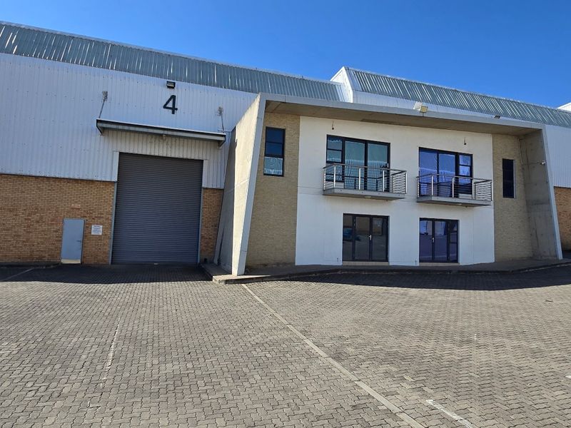 Front elevation of an industrial warehouse unit featuring a large roller shutter door, brick and metal cladding, and integrated office balconies.