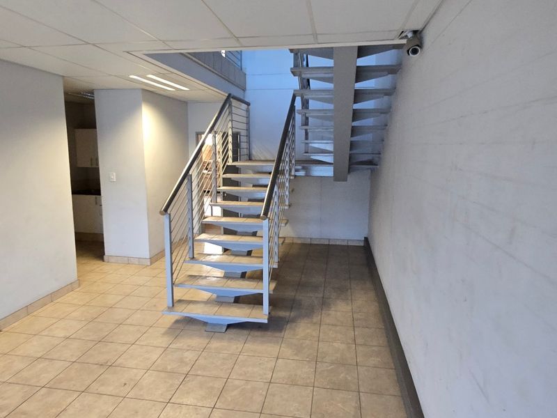 Spacious industrial hallway featuring a central metal staircase with stainless steel balustrades, tiled flooring, and a suspended ceiling.