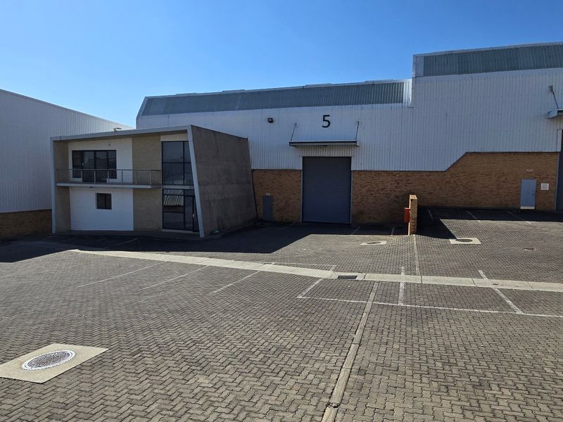 Exterior view of an industrial complex featuring multiple roller shutter doors, brick and metal cladding, and a paved parking area.
