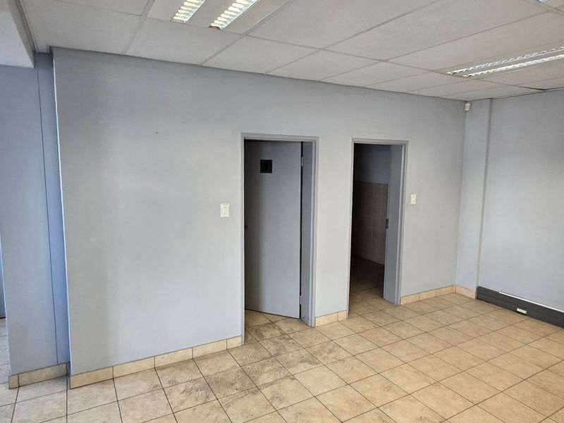 An empty industrial office space featuring tiled flooring, suspended ceilings with integrated lighting, and multiple internal access doors.