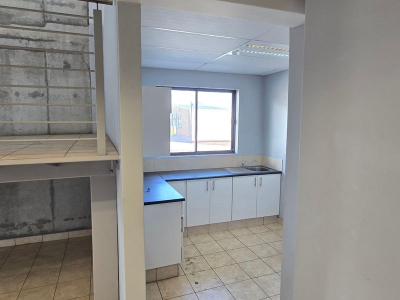 A functional kitchen area featuring built-in cabinetry, laminate countertops, and a stainless steel sink, adjacent to an industrial-style metal staircase.