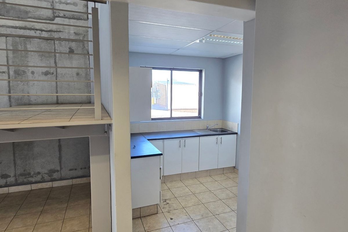 A functional kitchen area featuring built-in cabinetry, laminate countertops, and a stainless steel sink, adjacent to an industrial-style metal staircase.