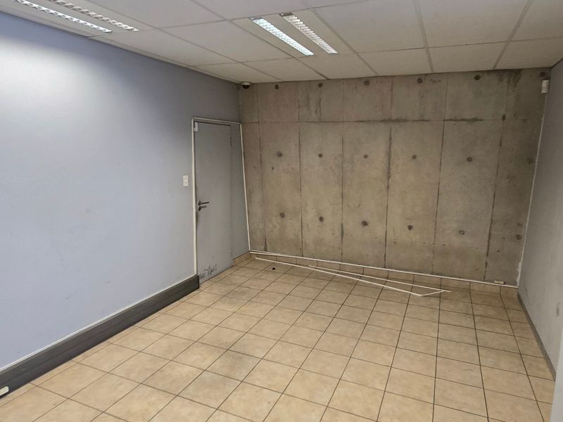 An empty office space featuring a combination of painted walls, an exposed concrete feature wall, ceramic tiled flooring, and a suspended ceiling with integrated lighting.