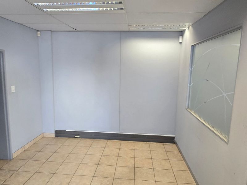 A clean, empty office space featuring ceramic floor tiles, a suspended ceiling with recessed lighting, and a frosted glass partition wall.