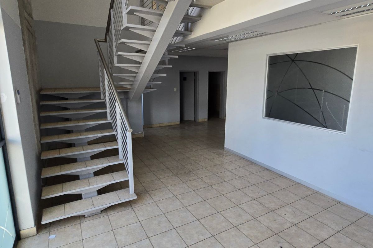 Spacious industrial entry area featuring a metal staircase, tiled flooring, and large windows, providing a bright and functional reception or transition space.