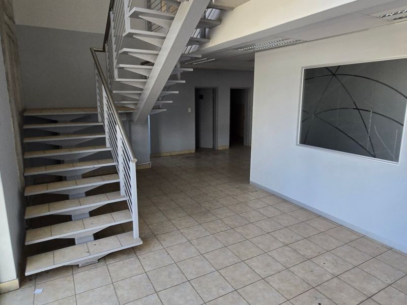 Spacious industrial entry area featuring a metal staircase, tiled flooring, and large windows, providing a bright and functional reception or transition space.