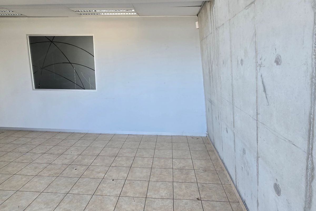 An empty industrial office space featuring an exposed concrete feature wall, tiled flooring, and a suspended ceiling with recessed lighting.